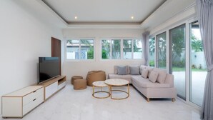 A modern living room with a sofa, television, and round coffee tables. - Orchid Paradise Homes OPV307 (Tambon Hin Lek Fai)