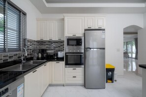 A modern kitchen with white cabinets, stainless steel appliances, and a tiled backsplash. - Orchid Paradise Homes OPV307 (Tambon Hin Lek Fai)