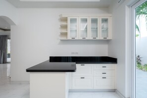 A modern kitchen with white cabinetry, black countertop, and a glass door cabinet. - Orchid Paradise Homes OPV307 (Tambon Hin Lek Fai)
