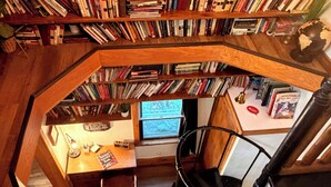 A multi-level library with bookshelves, a desk, and a spiral staircase. - The Schoolhouse Cabin - 2BR, 1.5BA with Hot Tub and Game Room (Hudson)