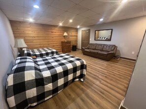 Una habitación con dos camas, un sofá, una pared de madera, un espejo y una lámpara.