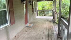 Une véranda en bois avec un ventilateur de plafond, un paillasson et une vue sur la verdure.