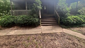Une maison à deux étages avec un porche à l’avant, un escalier menant à l’entrée et une pelouse bien entretenue.