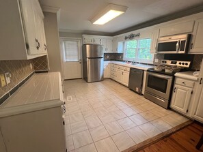 Una cocina con armarios blancos, electrodomésticos de acero inoxidable y piso de baldosas.