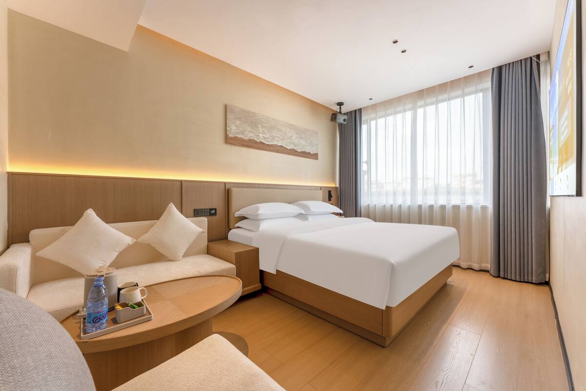 Una habitación de hotel moderna con una cama, un sofá, una mesita con una botella y un cuadro en la pared.