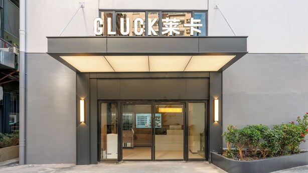 A modern building entrance with a glass door, illuminated by vertical lights, and a sign above reading 'GLUCK.'