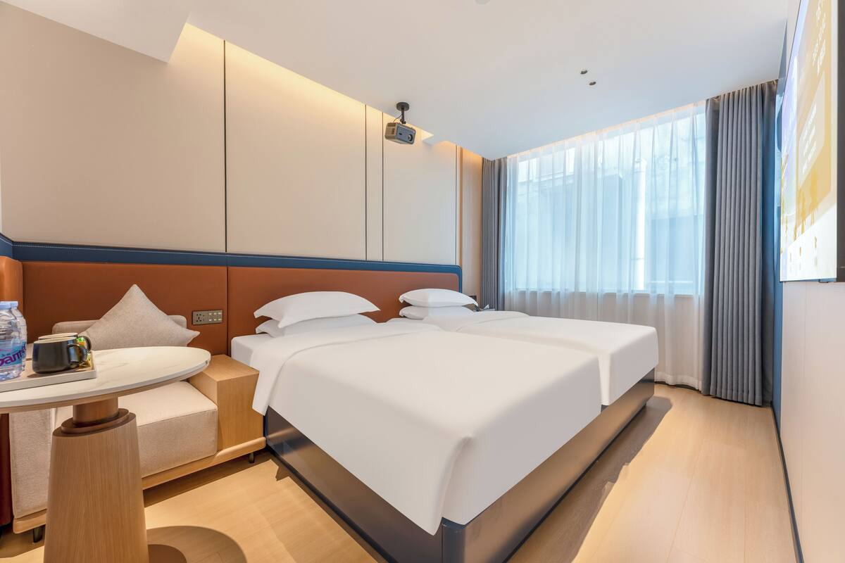 Una habitación de hotel con cama, mesita de noche y ventana con cortinas.