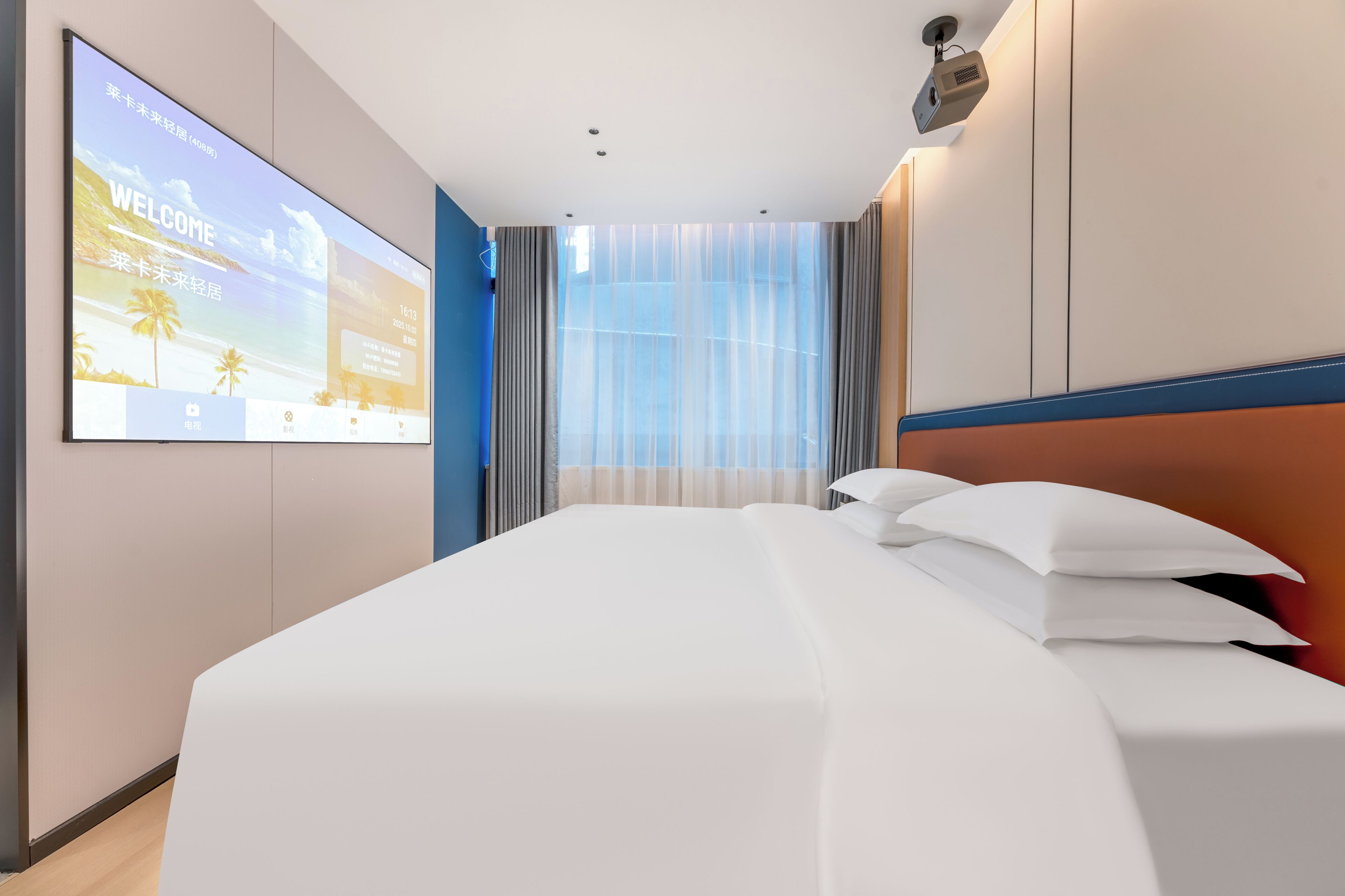 Habitación de hotel con una cama grande, una pantalla de televisión mostrando un mensaje de bienvenida, una ventana con cortinas y un proyector montado en el techo.