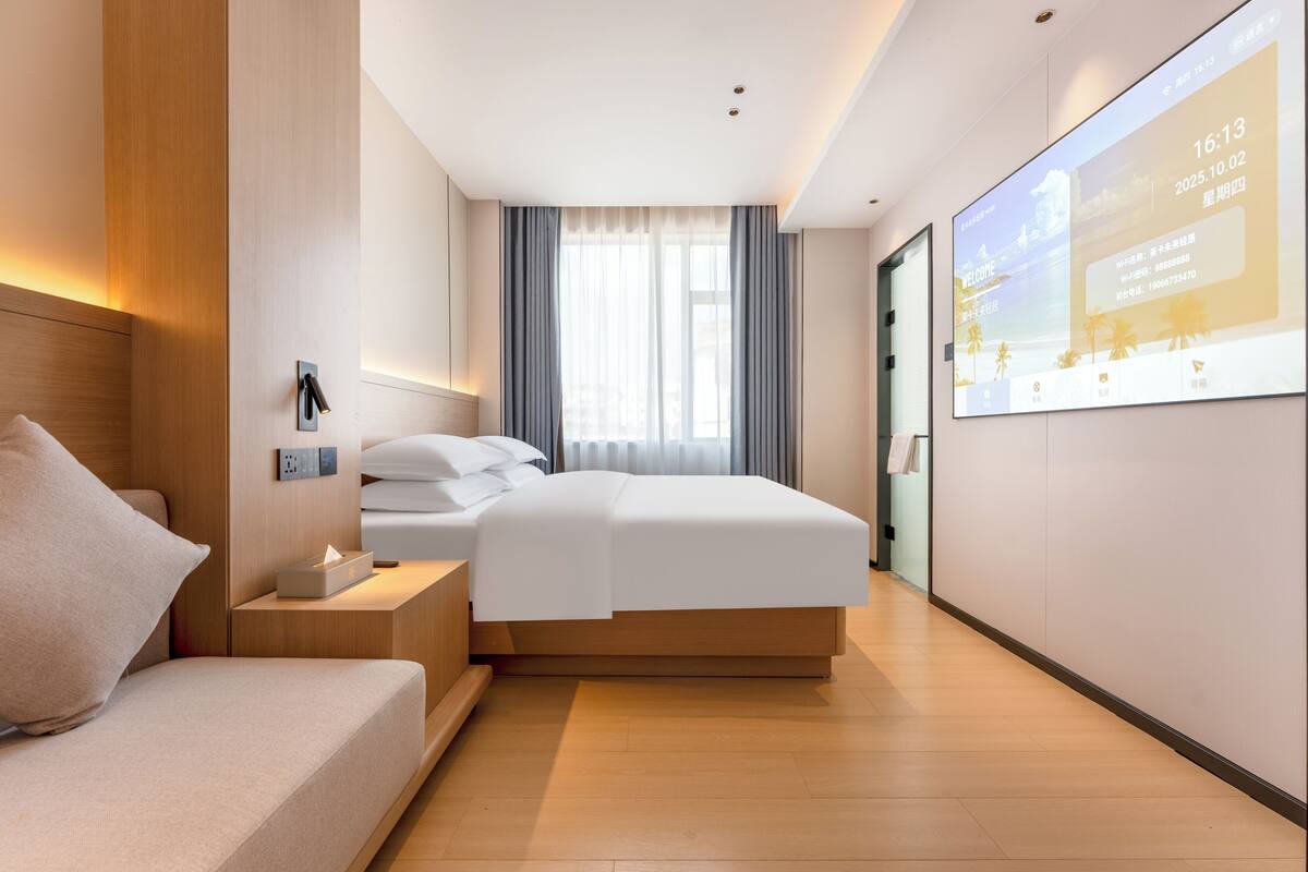 Una habitación de hotel moderna con cama, mesita de noche y una pantalla grande mostrando información.