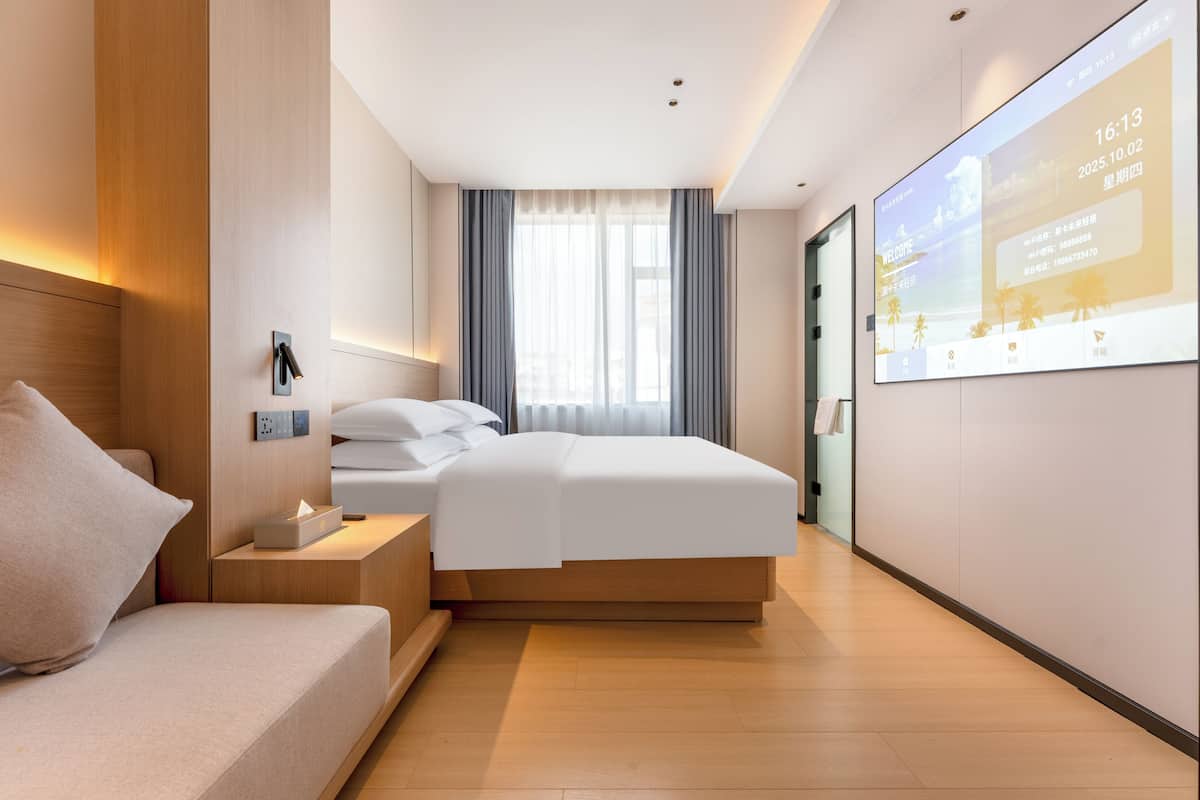 Moderni hotellihuone, jossa on sänky, yöpöytä ja suuri näyttö, jolla esitetään tietoa.