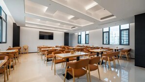 A spacious room with multiple tables and chairs, large windows, and a flat-screen TV mounted on the wall.