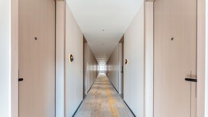 A long, narrow hotel corridor with doors on both sides, a patterned carpet, and a ceiling with recessed lighting.