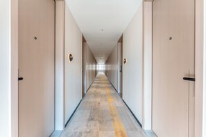 Pitkä, kapea hotellikäytävä, jossa on ovet molemmilla puolilla, kuvioitu matto ja upotetuilla valaisimilla varustettu katto.