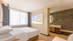 A modern hotel room with a bed, a desk, a chair, a bathroom with a mirror, and a TV screen displaying a welcome message.