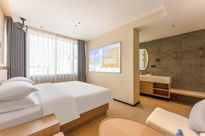 Moderni hotellihuone, jossa on sänky, työpöytä, tuoli, peilillä varustettu kylpyhuone ja televisio, jonka näytöllä näkyy tervetuliaisviesti.