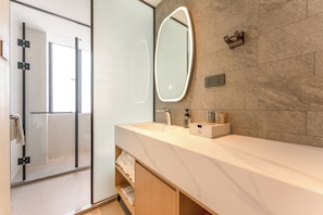A modern bathroom with a glass shower enclosure, a large mirror, and a marble countertop.