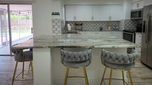 Una cocina moderna con armarios blancos, una isla de mármol y dos taburetes de bar.