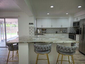 A modern kitchen with white cabinets, a marble island, and two bar stools. - Velara Naples, Beautiful Family Pool Home Near Beach & Downtown. (Naples)