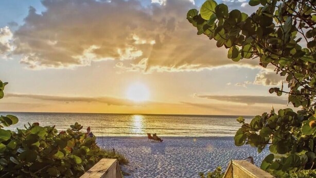 Una terraza de madera que conduce a una playa con un atardecer de fondo.
