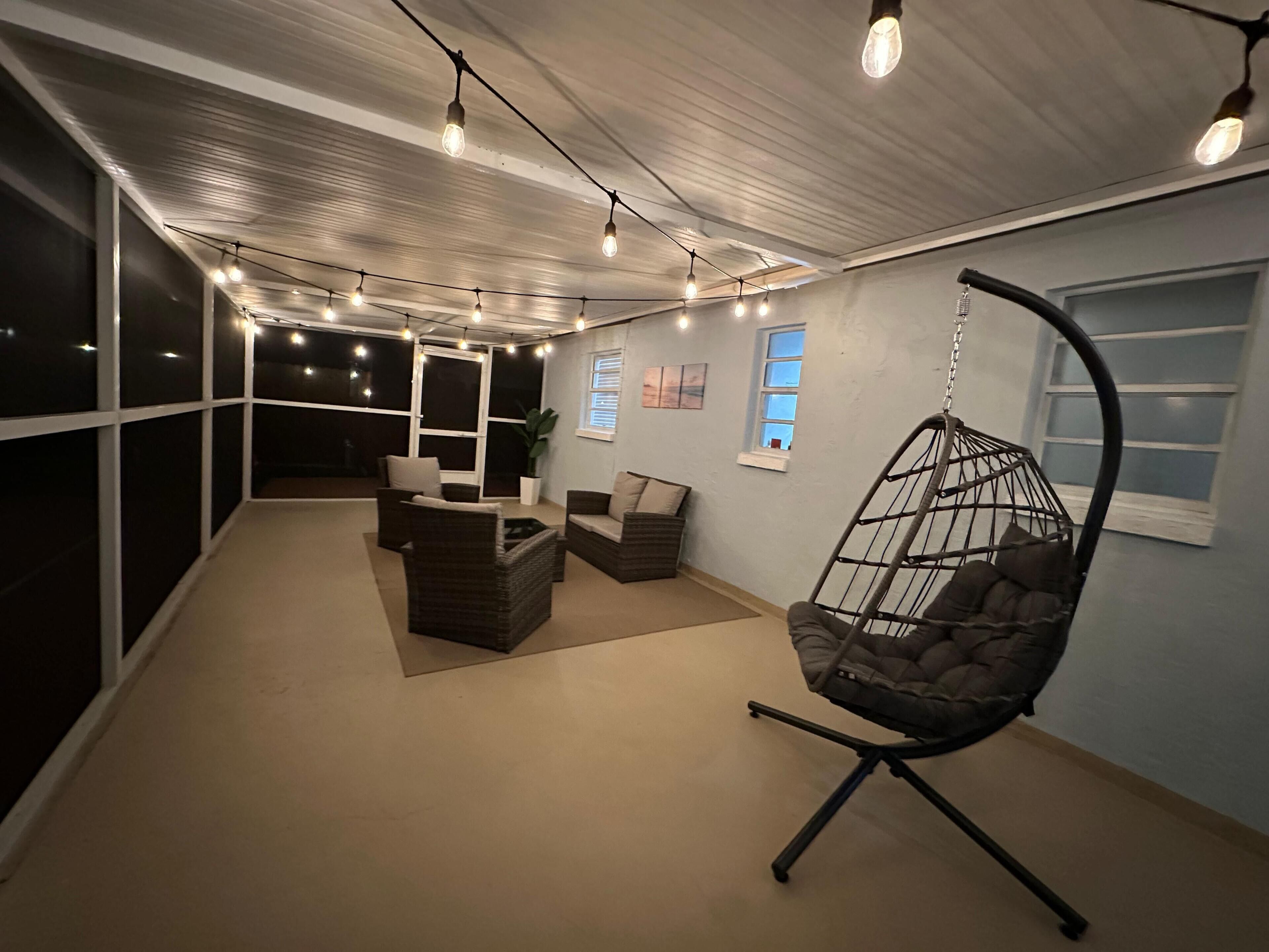 A room with a hanging chair, sofas, and string lights.