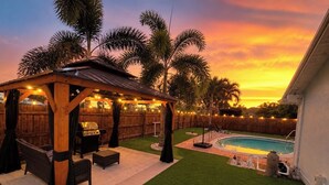 Un patio trasero con un porche de madera, una parrilla y una piscina.