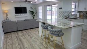 Una cocina moderna con una isla central, taburetes de bar, un sofá gris y un ventilador de techo.