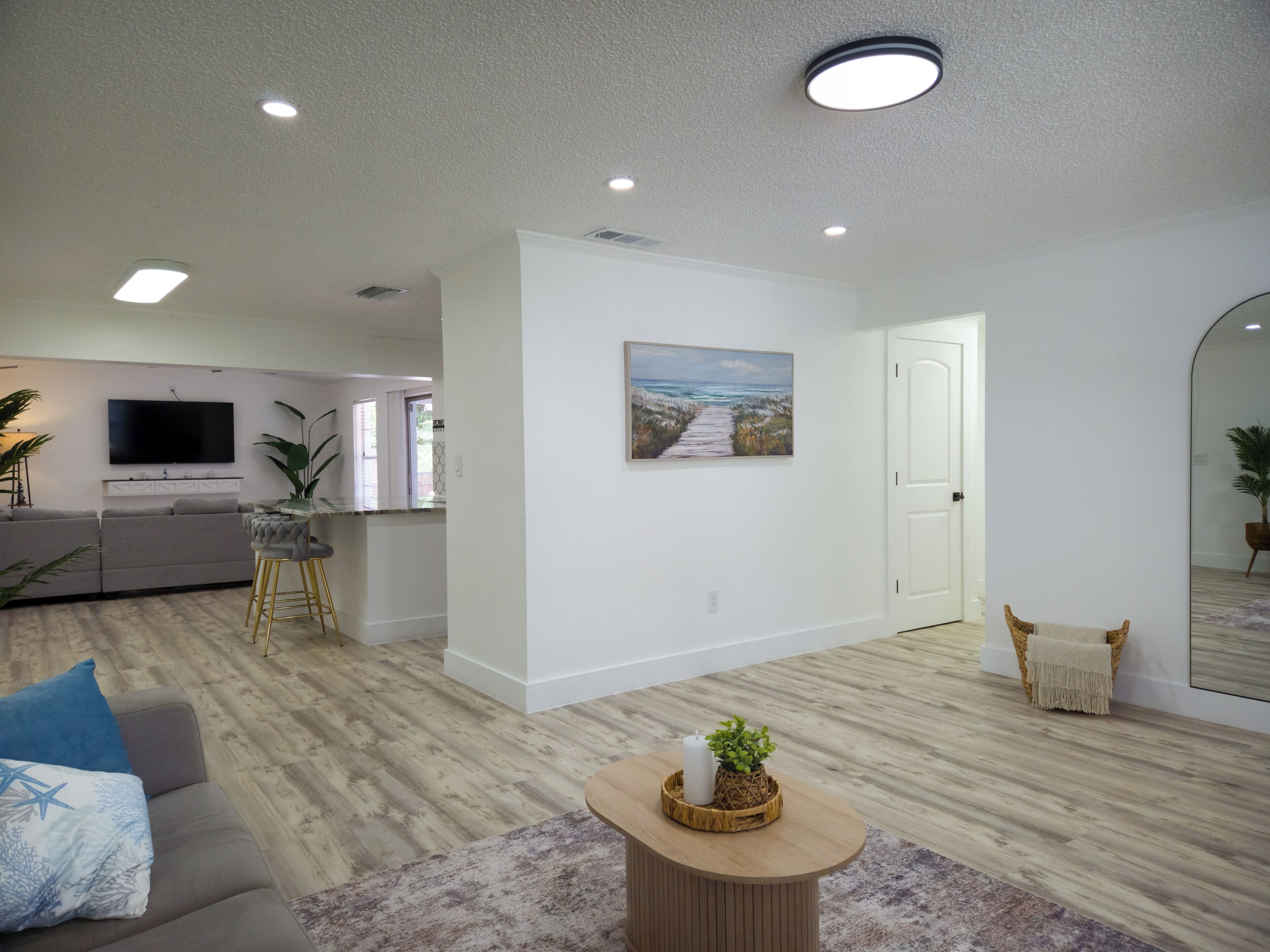 A modern living room with a sofa, a coffee table, a painting, and a kitchen area in the background.