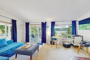 A modern living room with a sofa, ottoman, and chairs, a balcony with a view, and a television.