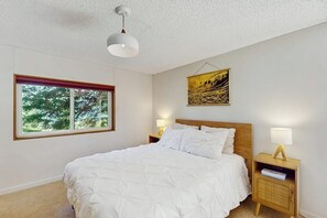 A bedroom with a bed, a window, a wall-mounted artwork, and bedside lamps.