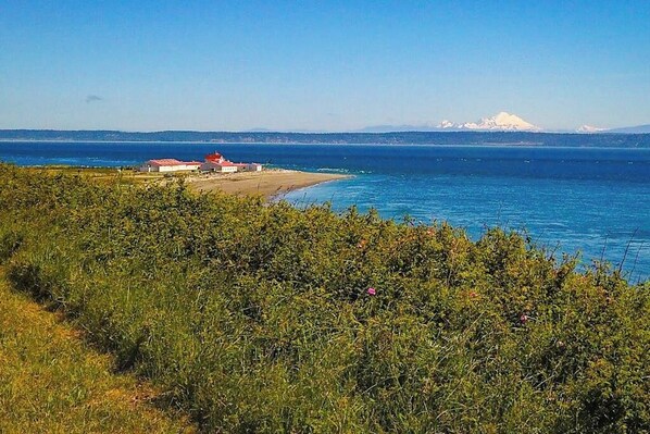 A coastal landscape with a building near the shore, a clear sky, and distant mountains.