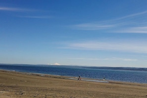A beach with a clear sky, a distant mountain, and a few people walking.