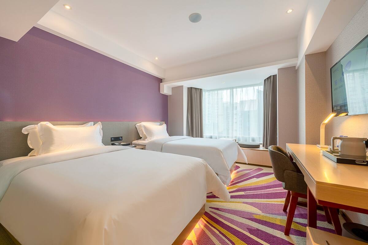 Habitación de hotel con dos camas, un escritorio y un ventanal grande con cortinas.