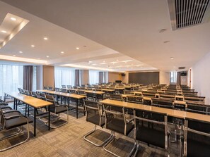 A conference room with rows of tables and chairs, large windows, and a projector screen.