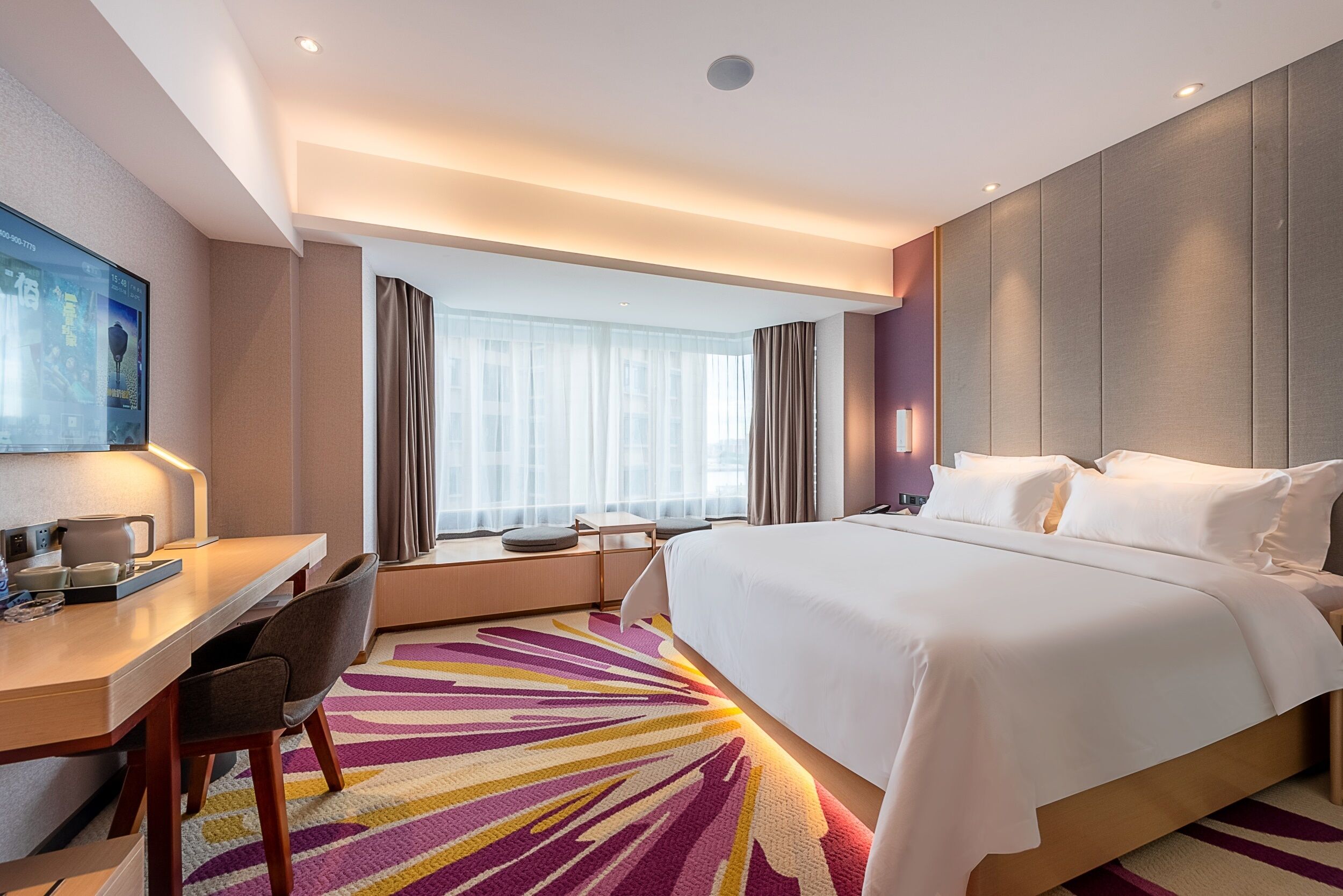Une chambre d’hôtel avec un lit, un bureau, des chaises et une grande fenêtre avec des rideaux.