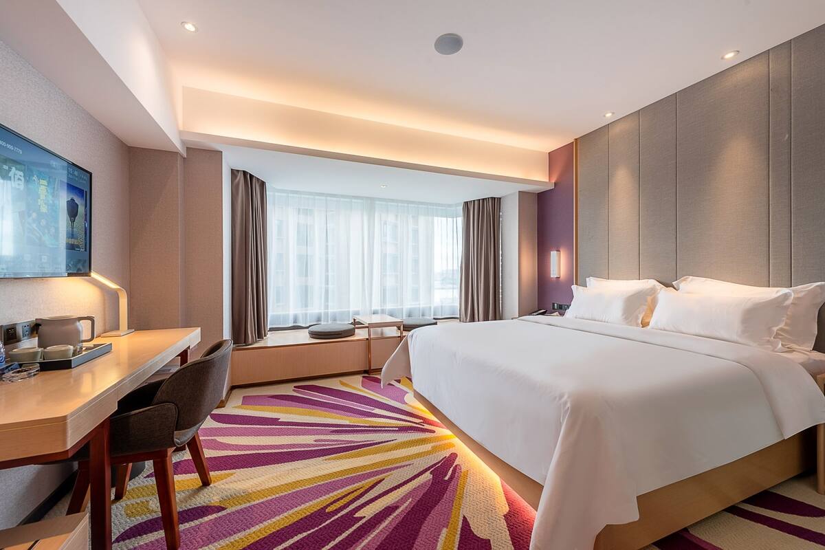 Una habitación de hotel con cama, escritorio, sillas y un ventanal con cortinas.