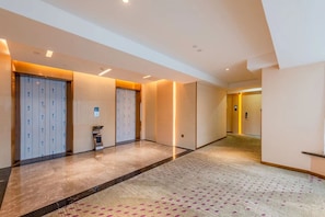 Un pasillo de hotel con piso alfombrado, un ascensor de vidrio y una puerta con un cartel.
