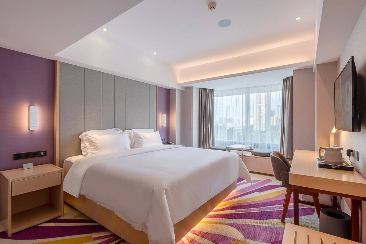 Una habitación de hotel con cama, mesita de noche, escritorio, silla y un ventanal con vistas a la ciudad.