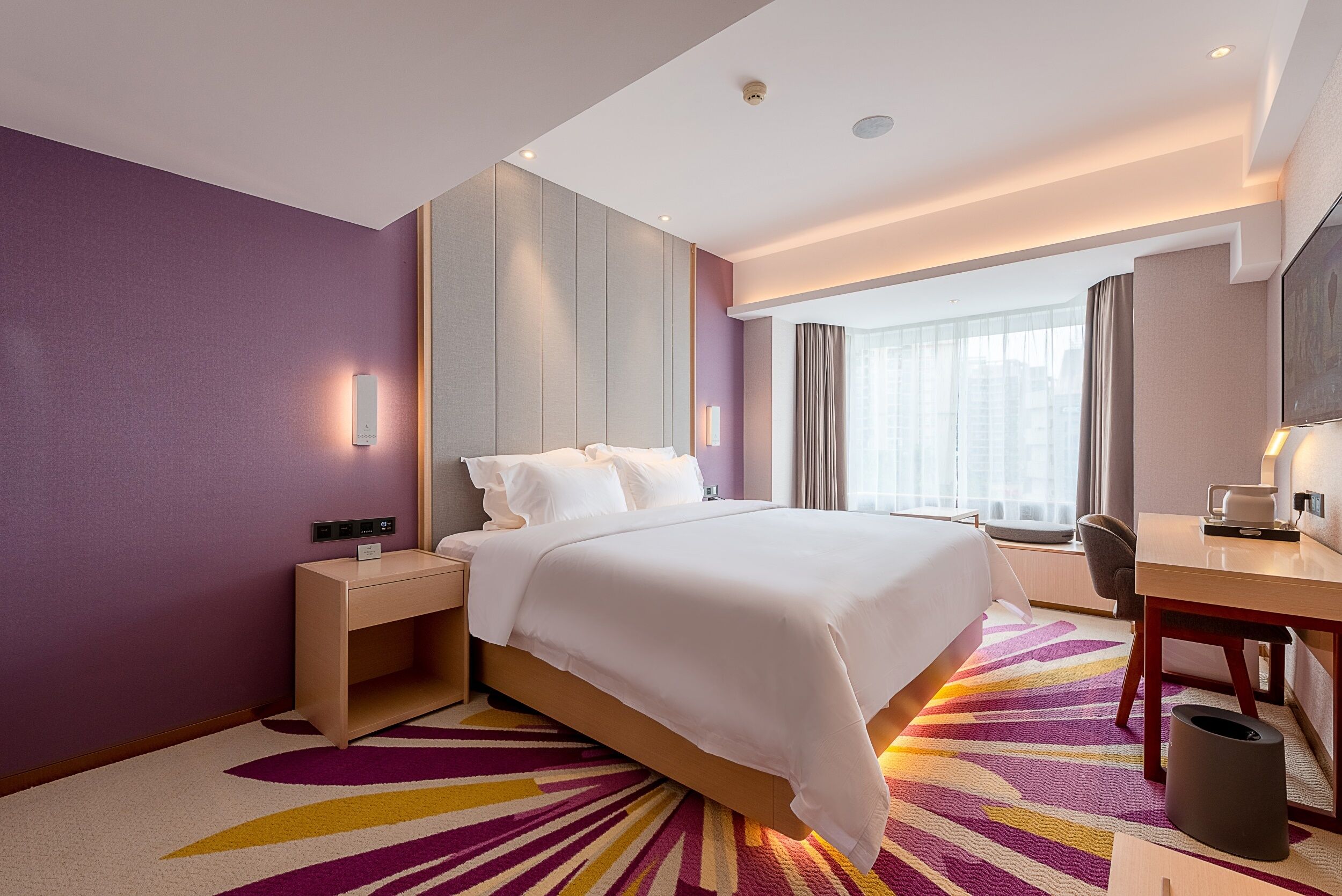 Une chambre d’hôtel avec un lit, une table de chevet, un bureau et une vue sur la ville.