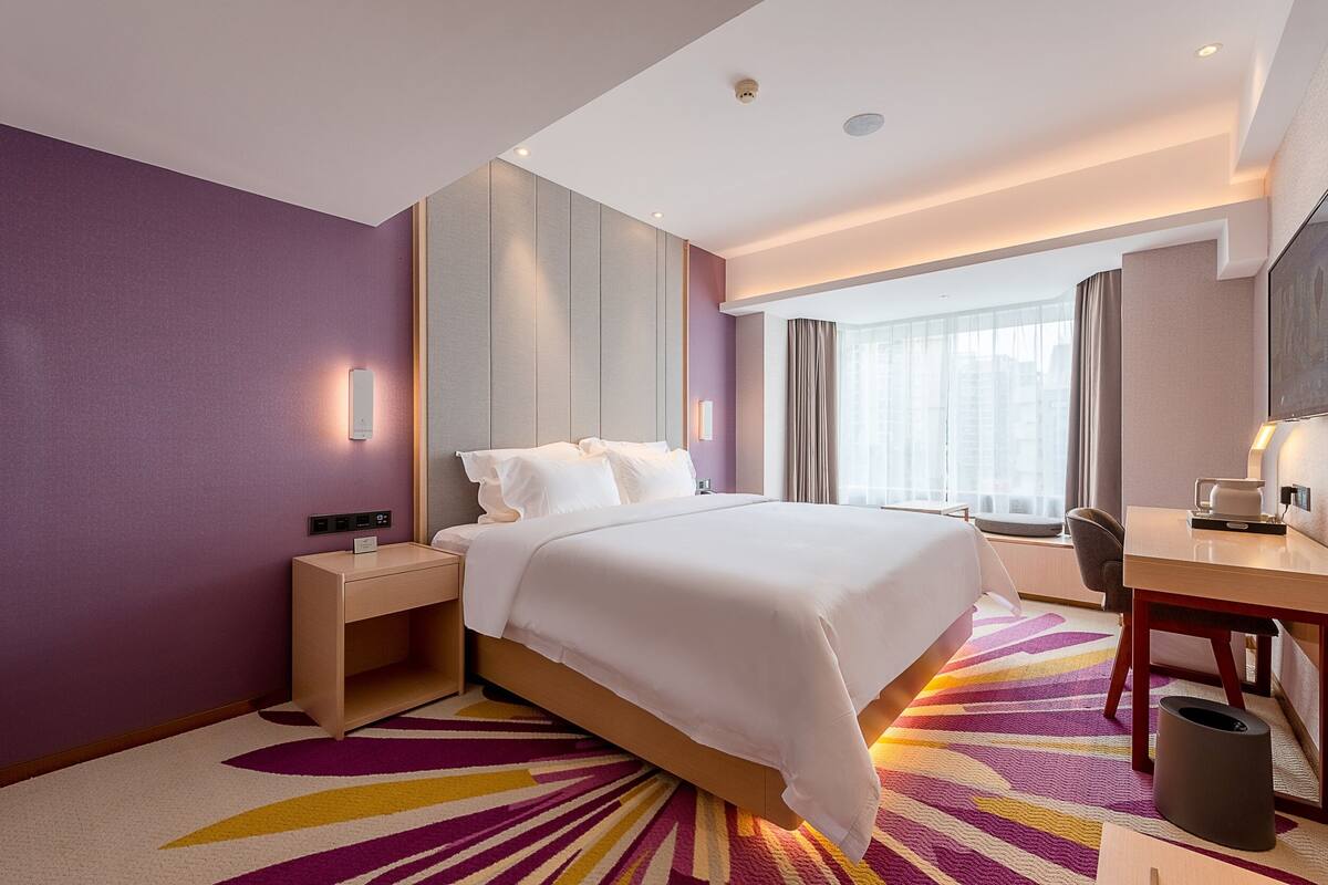 Habitación de hotel con cama, mesita de noche, escritorio y vistas a la ciudad.