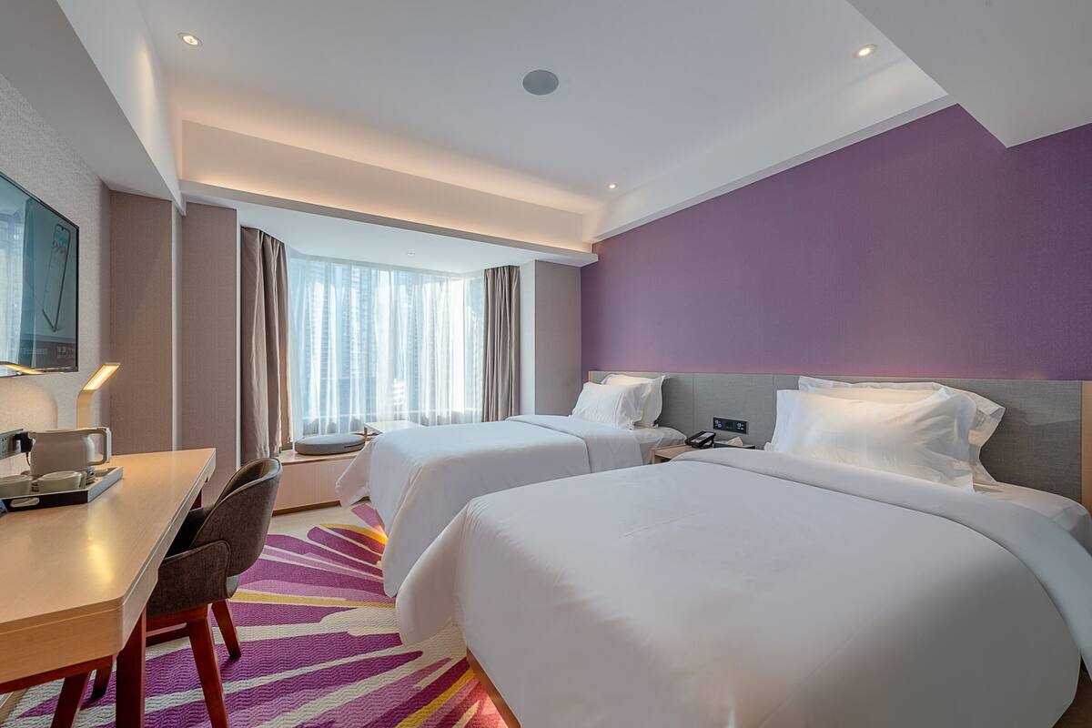 Habitación de hotel con dos camas, un escritorio, una silla, un televisor y una ventana con cortinas.