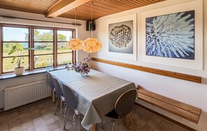 Uma sala de jantar com mesa, cadeiras, janela com vista e quadros na parede.