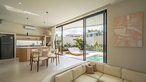 Una cocina moderna con comedor, una sala de estar con sofá y un amplio ventanal con vista a una piscina.