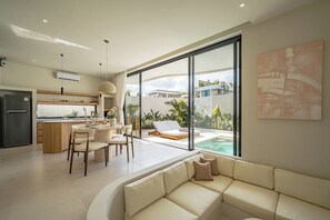 Una cucina moderna con zona pranzo, un soggiorno con divano e vista su una piscina.