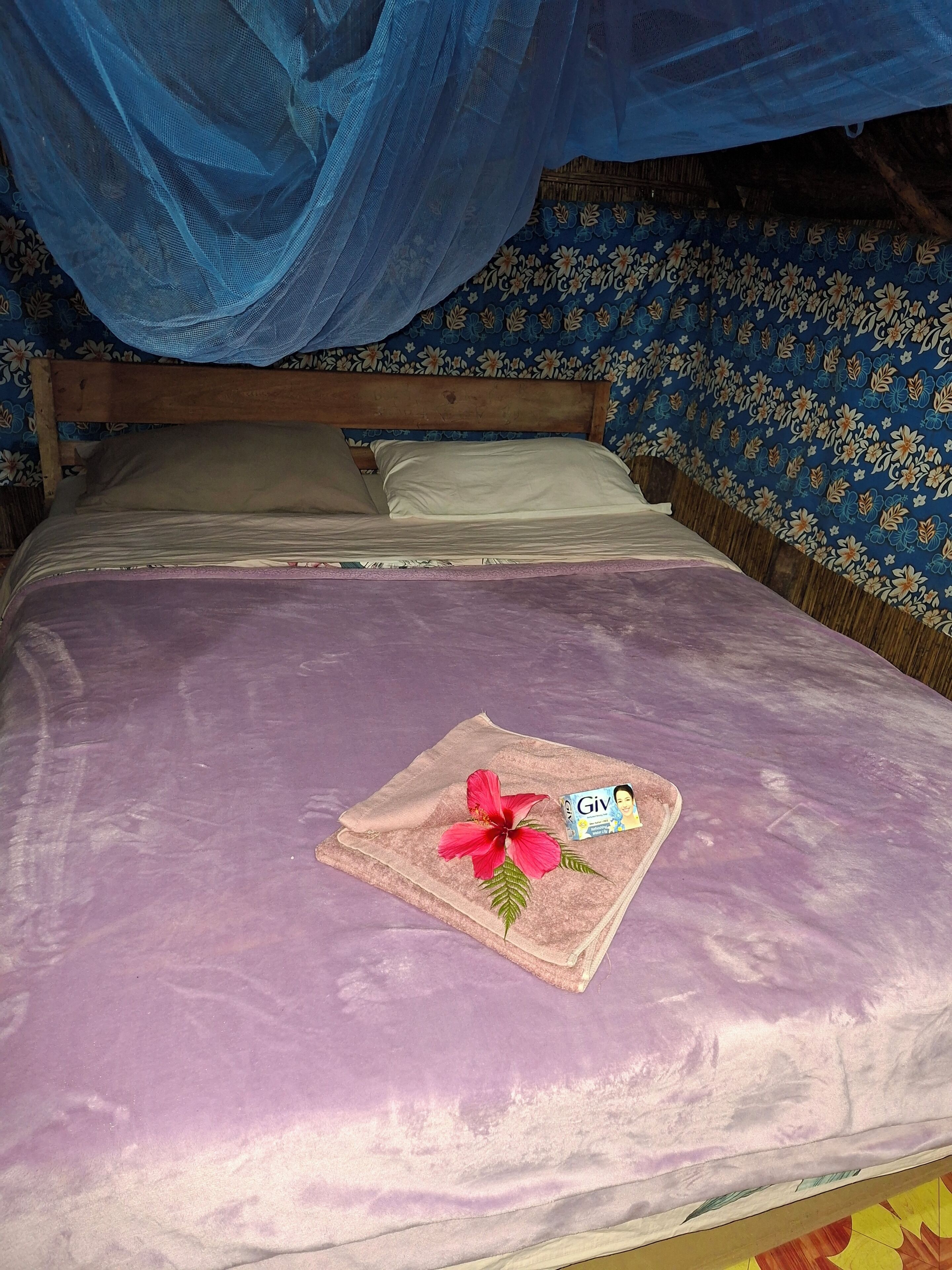 A bed with a purple bedspread, a blue mosquito net, and a floral-patterned wall.