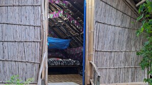 Una struttura rustica in legno con tetto di paglia, una scala in legno che conduce a un letto con coperta a motivi zebrati e un muro in bambù.