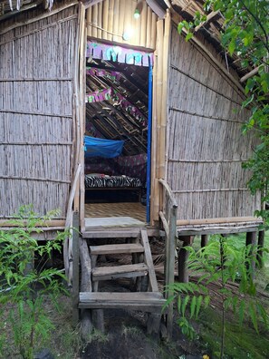 Une structure rustique en bambou, dotée d’un escalier en bois menant à un lit recouvert d’une couverture à motifs zébrés.
