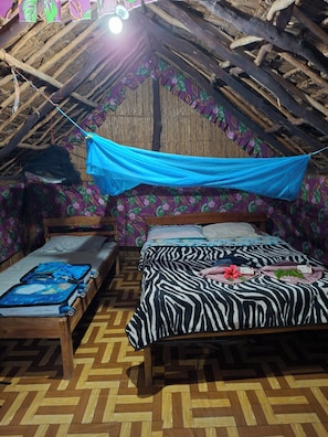 A room with a thatched roof, two wooden beds, a patterned wall, and a blue canopy.