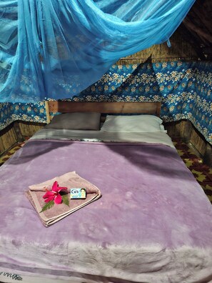 A bed with a purple bedspread, a pink hibiscus flower, and a baby bottle.