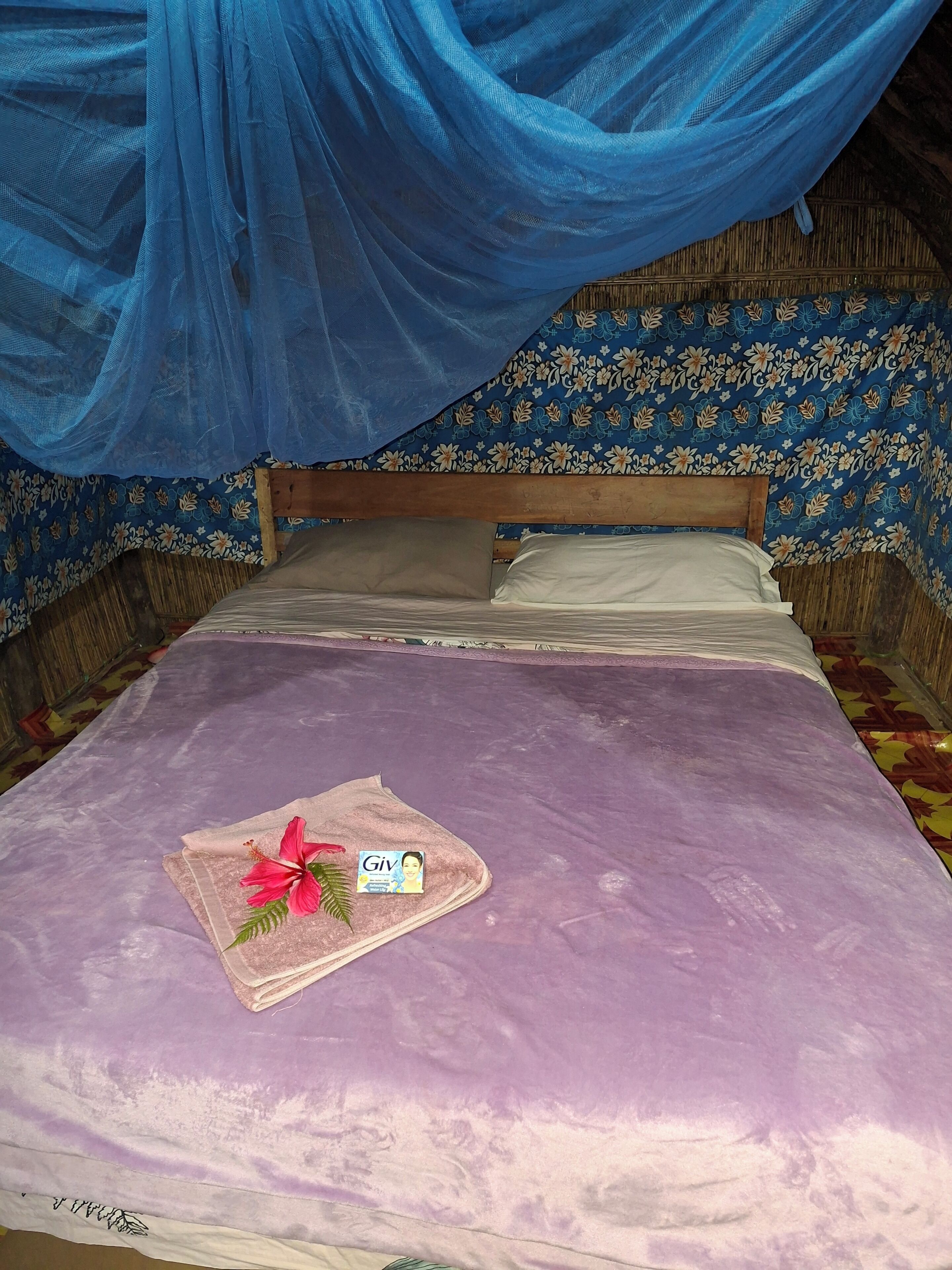Una cama con una colcha morada, una toalla rosa con una flor de hibisco y una tarjeta de 'Giv'.