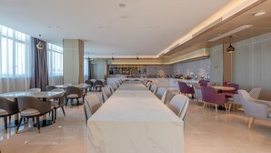 Un vaste espace de restauration d’hôtel, doté d’un long comptoir en marbre, de plusieurs types d’aménagements pour s’asseoir et d’une cuisine moderne en arrière-plan.